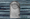 A gray tombstone with a background of stacked newspapers.