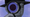 A person in a fedora with a magnifying glass up to their eye, with a purple background