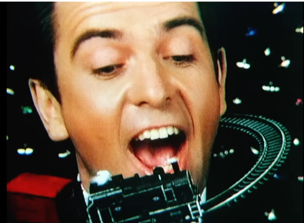 Peter Gabriel's face, mouth agape, with a tiny steam locomotive circling his head. From the seminal music video for "Sledgehammer." 