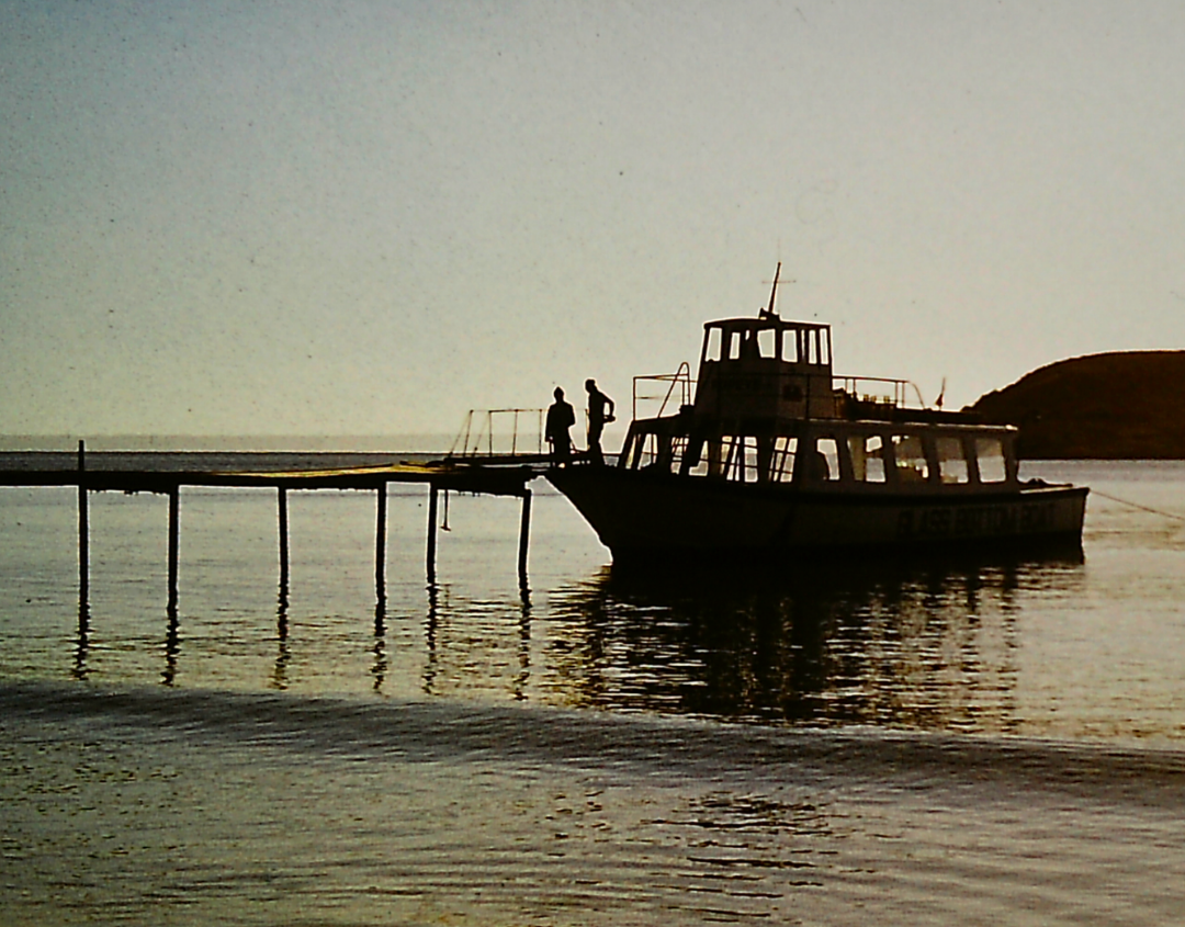 An old photo of two people stood on a boat at a jetty