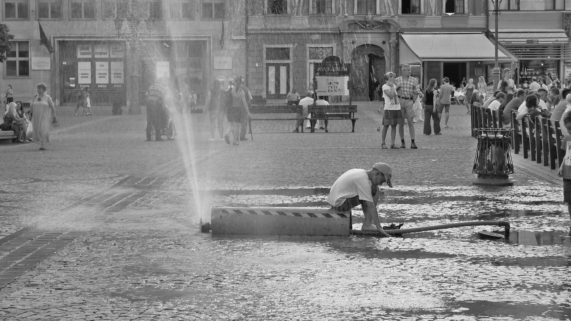 A photo of a boy sitting in Wroclaw town square with water spraying around