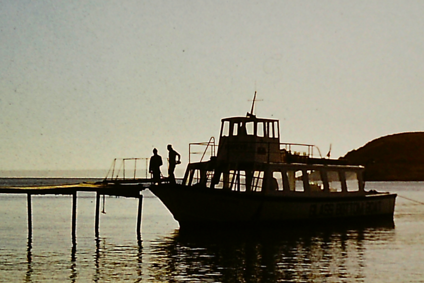 An old photo of two people stood on a boat at a jetty