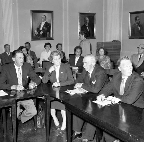 An old photo of people meeting in a town hall meeting - from Enligt notering: "Möte på Rådhuset Socialmötet maj -60". by Andersson, Arne - Bohuslän Museum, Sweden - Public Domain.