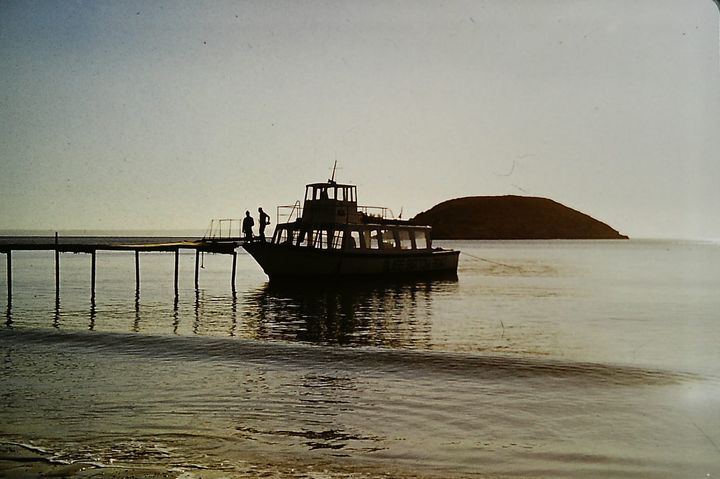 An old photo of a boat mooring at a pier with sun setting behind