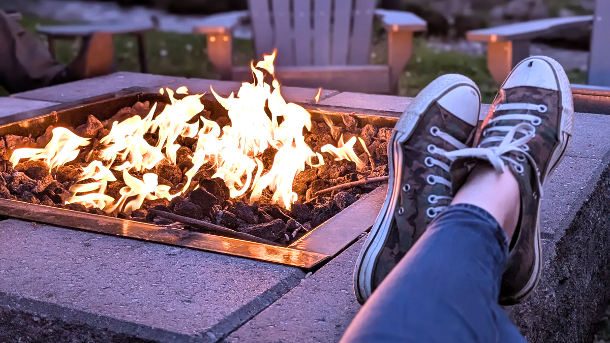 Square fire pit with a low fire, camo Converse sneakers on crossed ankles, propped by by the edge.