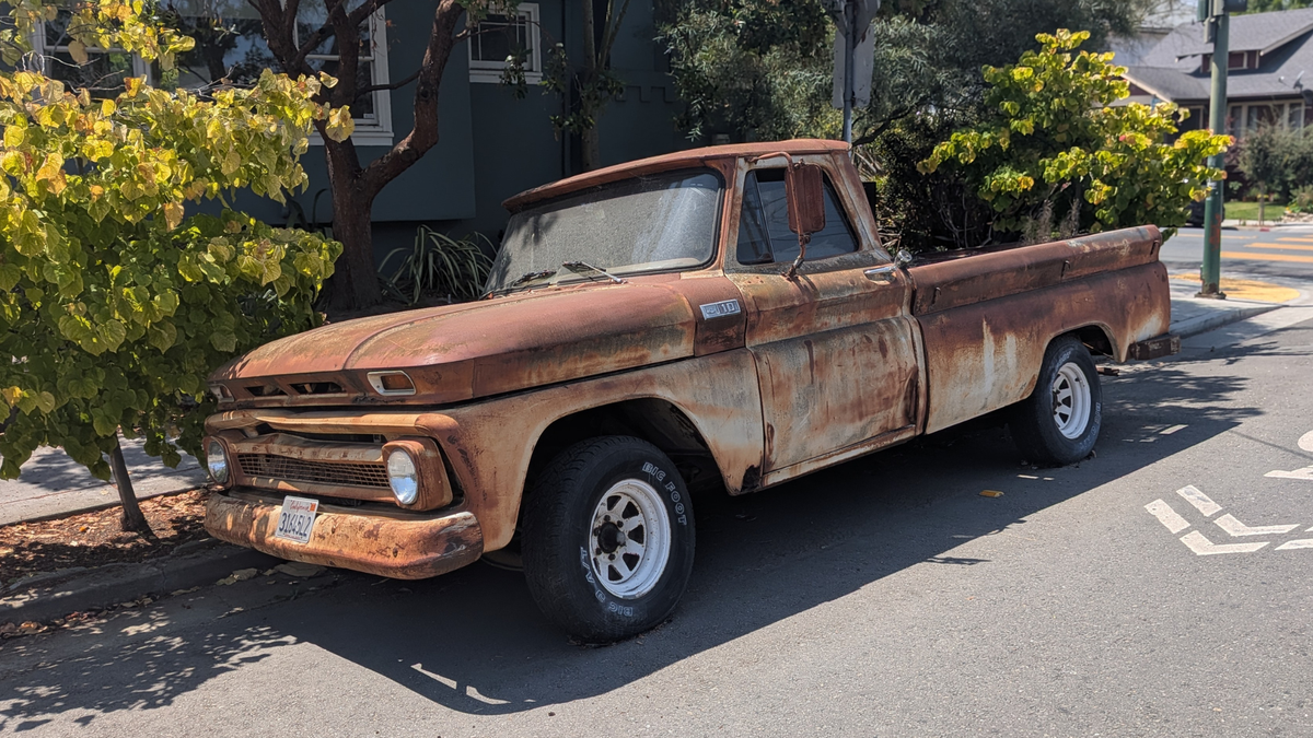 A late 1950s model pickup truck, completely rusted out, sitting on the curb in Oakland.