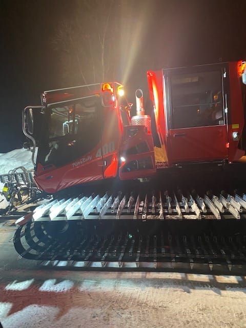 The Petersville Community NPC's snowcat, Angel, works in the dark on a snowy trail.
