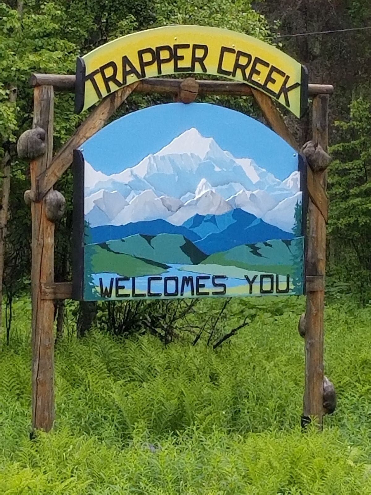 A wooden roadside sign welcomes visitors to Trapper Creek, Alaska