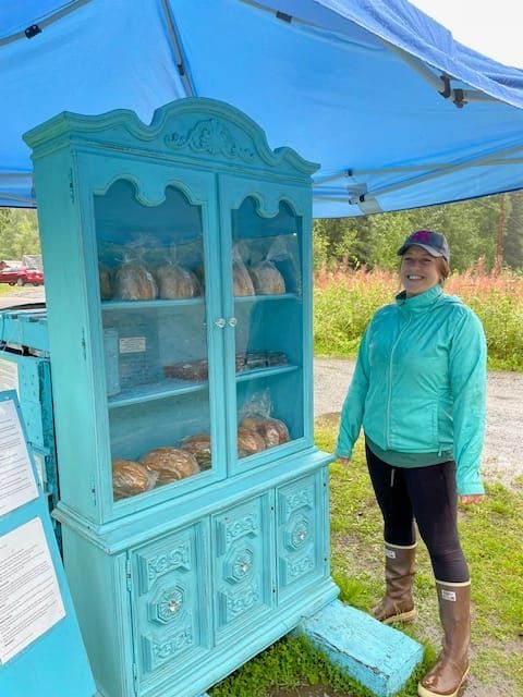 Renee Gunderson stands next to her little teal hutch full of sourdough goodies at Mile 115 on the Parks Highway.