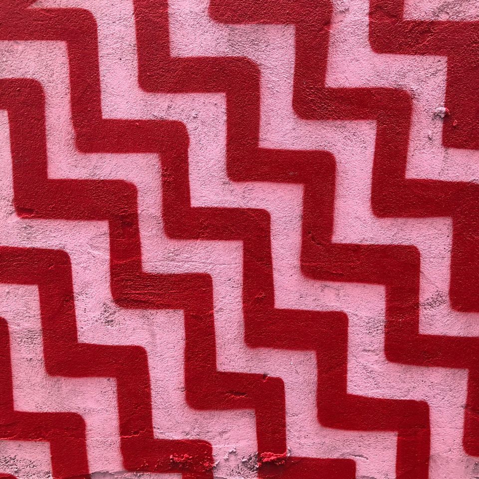 red and pink painted lines zig zag across a cement wall