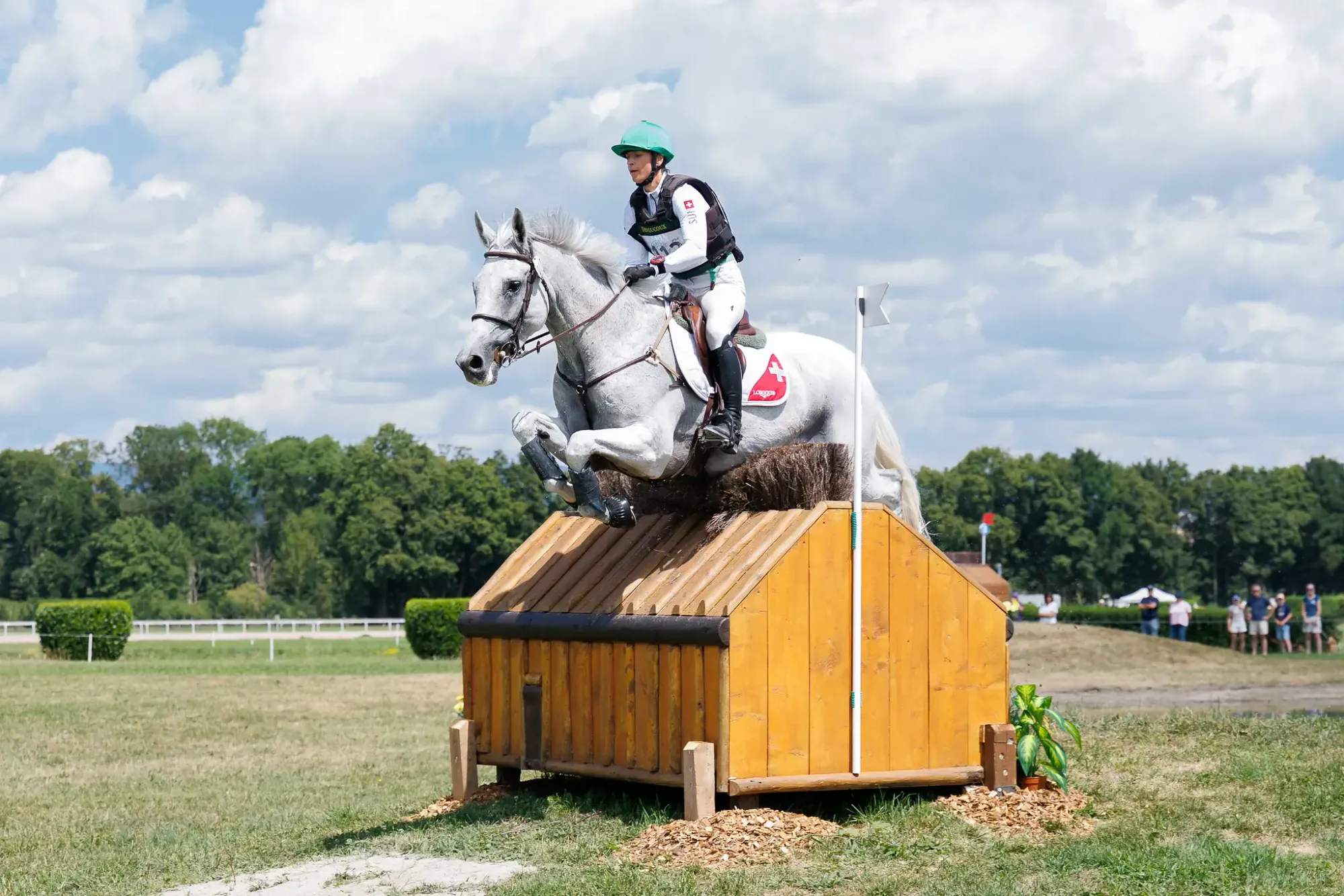 Binomio con manta de la bandera suiza salta un obstáculo de madera durante la prueba de cross country en Avenches.
