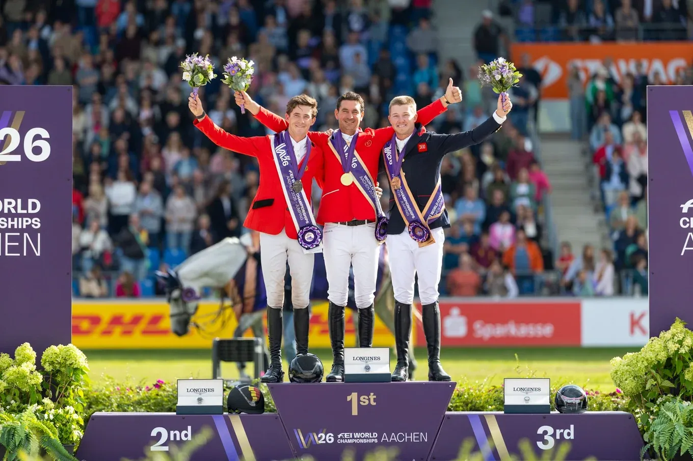 Steve Guerdat, Thibeau Spits y Harry Charles levantan ramos de flores en el podio individual del Mundial de Salto de Aachen 2026.