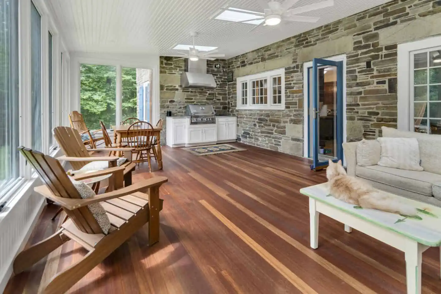 Sunlit patio with cozy seating, stone grill wall, and lounging cat on coffee table.