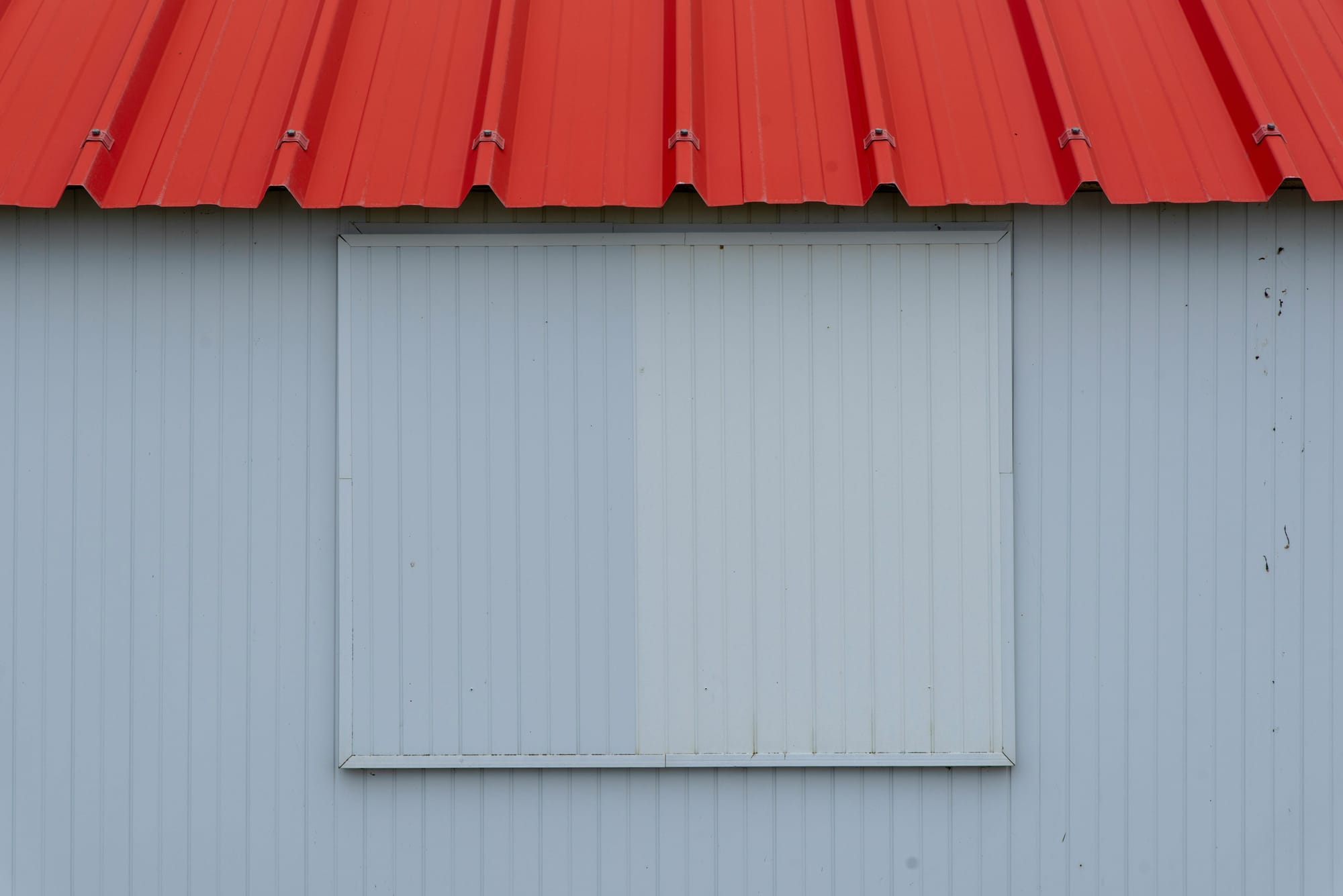“Detail of a red metal roof edge above blue-gray corrugated exterior panels.”