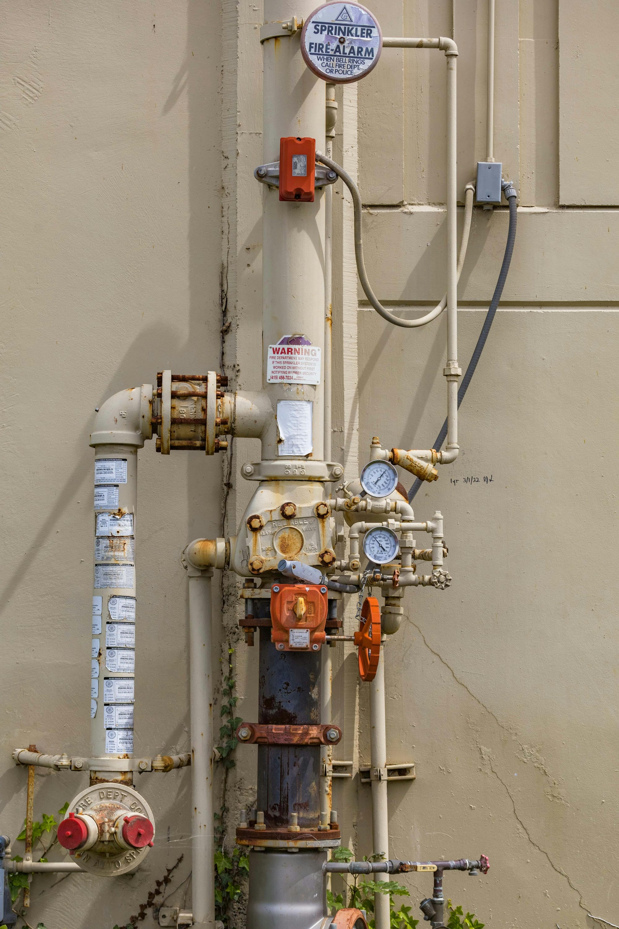 Fire sprinkler alarm and valve assembly with pipes and pressure gauges mounted on an exterior wall.