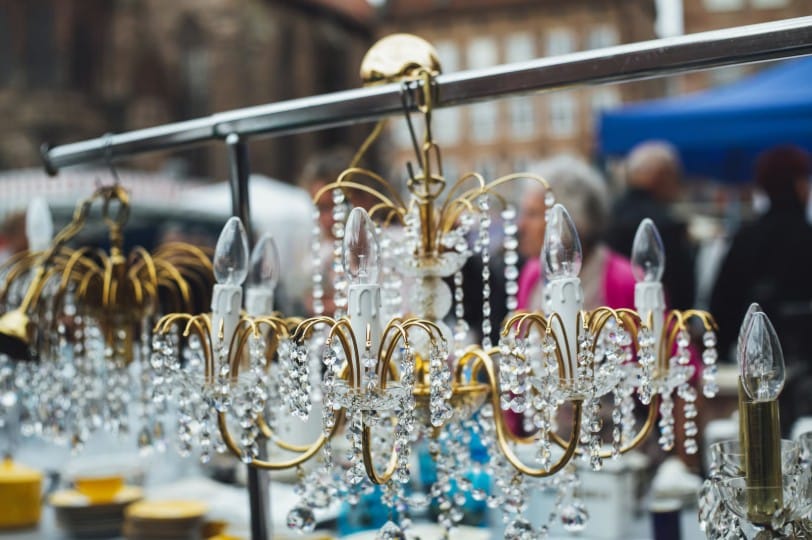 Vintage gold-framed crystal chandeliers with candle-style bulbs hanging from a metal display rack at an outdoor market.