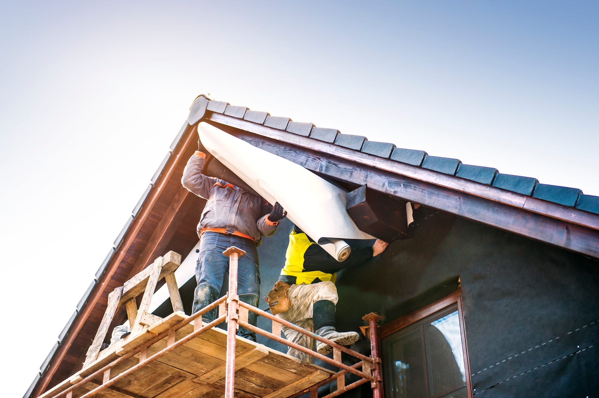 Workers repairing an aging, worn-out roof on a home.