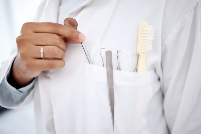Dental professional with examination tools and a toothbrush inside their lab coat pocket.