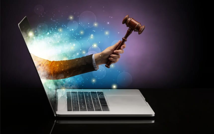A conceptual illustration of a hand reaching out of a laptop screen holding a wooden judge's gavel amidst glowing digital lights, representing online legal services.