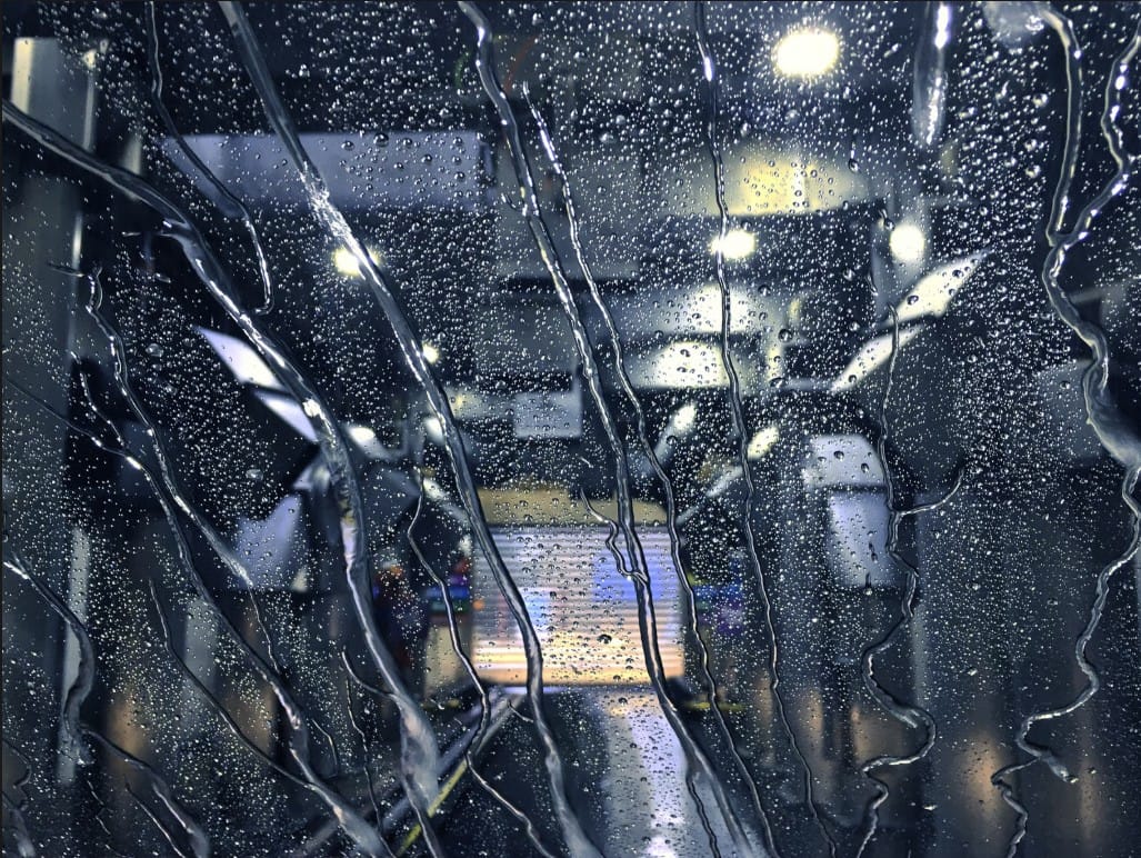 Water droplets streaming down a vehicle windshield inside an automatic car wash.