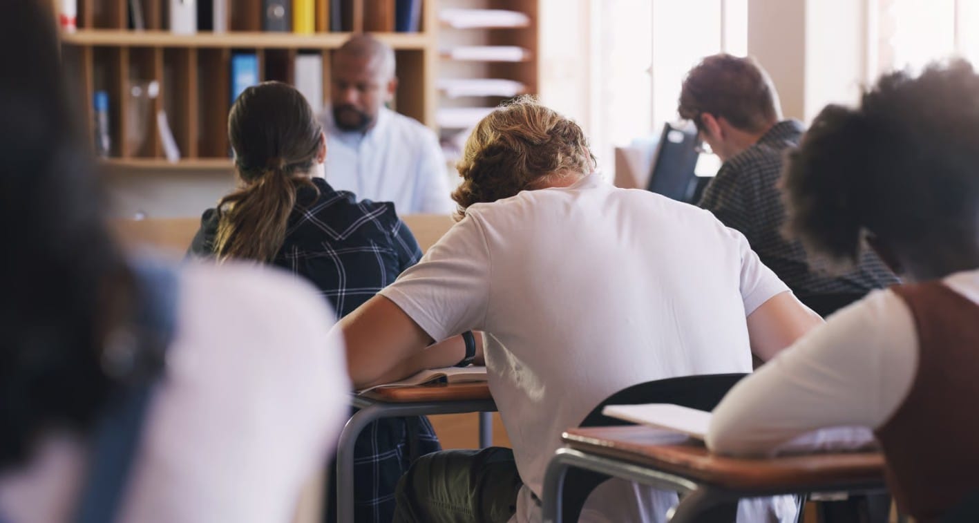 Students sitting at desks taking notes during a classroom lecture.