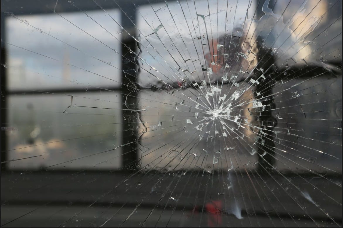 Close-up of a broken glass pane showing a radial crack pattern from an impact point.