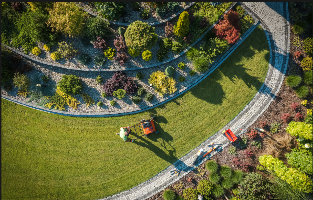Professional lawn care service mowing a manicured lawn next to stone pathways and terrace gardens.