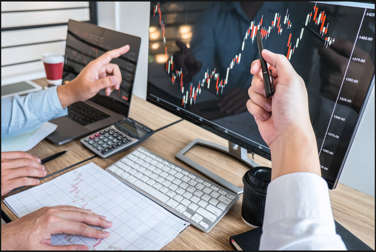 Financial analysts pointing at stock market candlestick chart performance on a desktop computer screen.