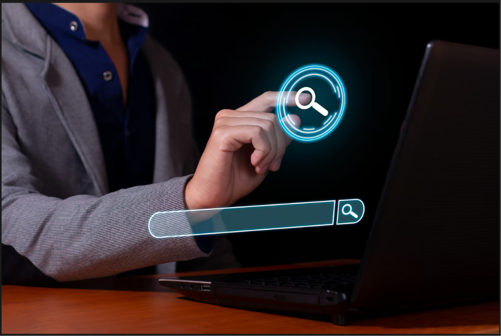 Professional in a blazer touching a glowing digital search icon above a search bar overlay beside a laptop.