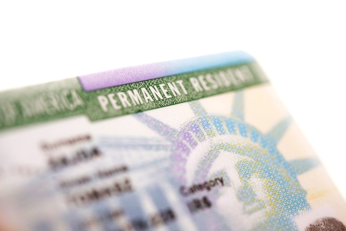 Close-up of a U.S. Permanent Resident Card showing the words ‘PERMANENT RESIDENT’ with part of the Statue of Liberty’s crown in the background.