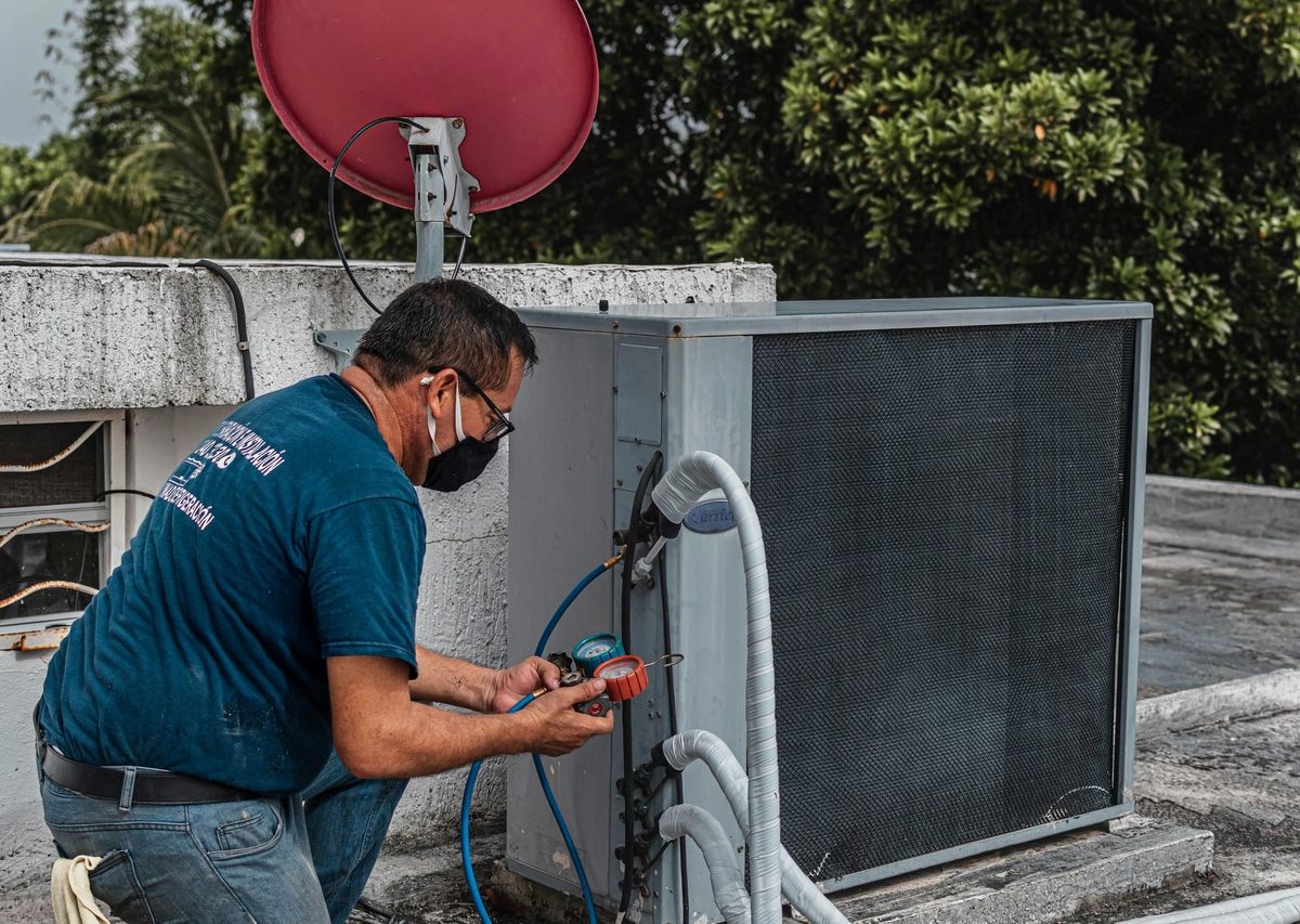 HVAC technician inspecting and servicing an outdoor air conditioning unit on a rooftop