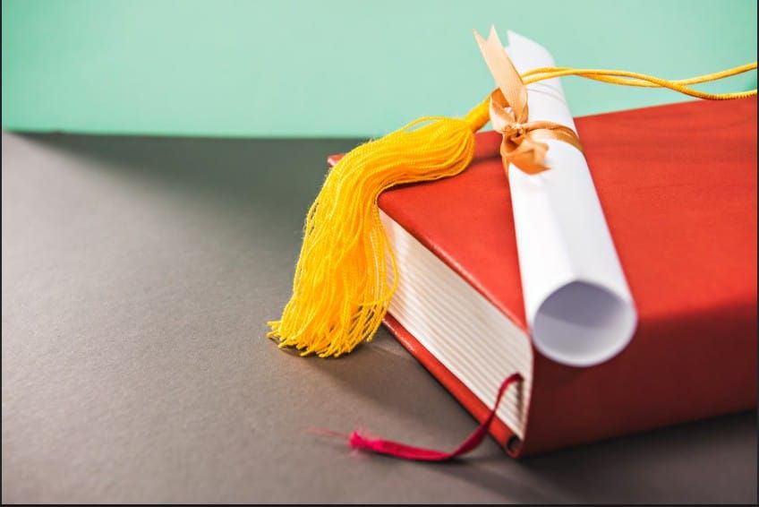 A graduation diploma and tassel on a textbook, representing academic success, graduation day, and higher education milestones.