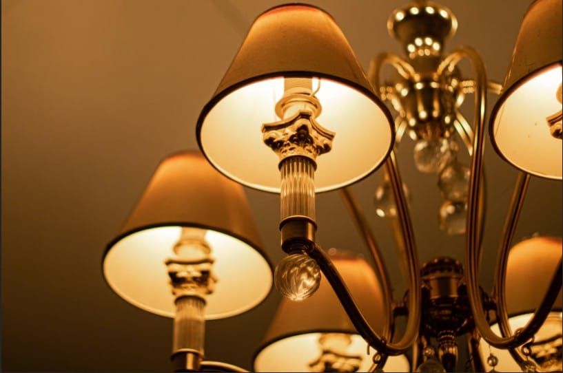  Low-angle view of a classic brass chandelier with multiple arms and warm, illuminated fabric lampshades against a neutral ceiling.