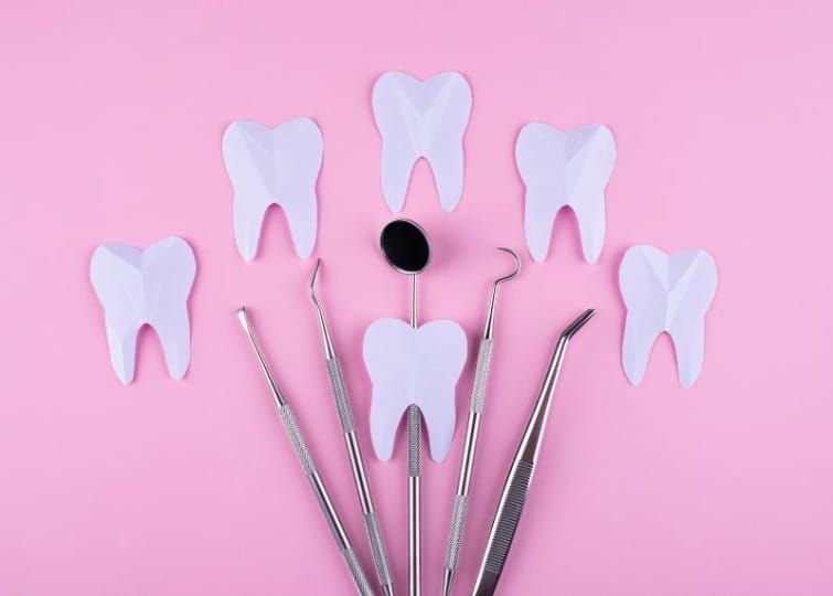 Flat lay of professional dental tools including a mouth mirror and tweezers, surrounded by paper tooth shapes for oral health concepts.