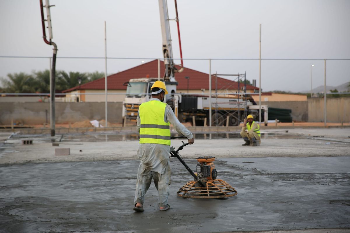 Concrete contractor using a power trowel to finish a newly poured slab.