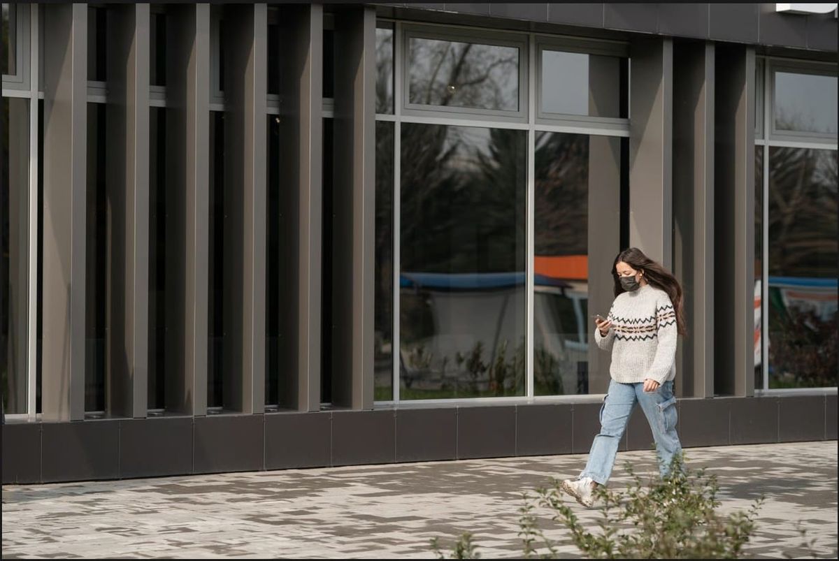 Woman walking past a modern building exterior featuring dark tinted glass windows for privacy and solar protection.