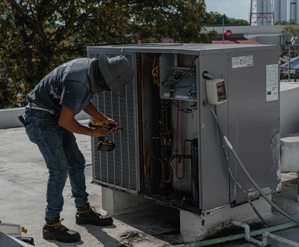 Technician inspecting a rooftop HVAC unit, checking coils and wiring, representing indoor air quality Bay Area services
