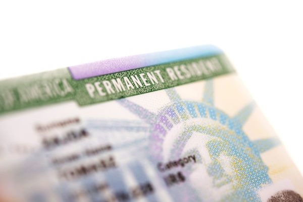 Close-up of a U.S. Permanent Resident Card showing the words ‘PERMANENT RESIDENT’ with part of the Statue of Liberty’s crown in the background.