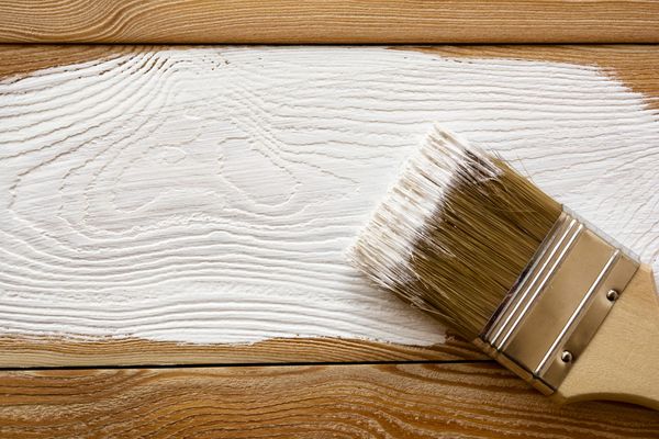 A paintbrush resting on a wooden surface with a fresh stroke of white paint, highlighting the wood grain.