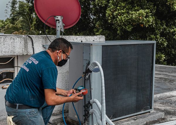 HVAC technician inspecting and servicing an outdoor air conditioning unit on a rooftop