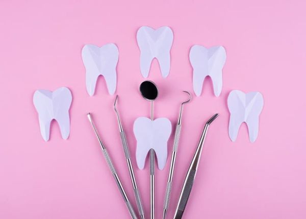Flat lay of professional dental tools including a mouth mirror and tweezers, surrounded by paper tooth shapes for oral health concepts.