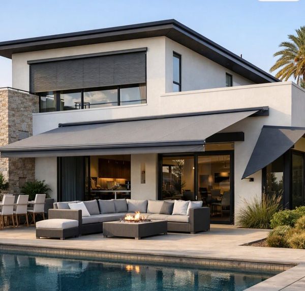 Luxury modern home exterior with retractable patio awning, outdoor furniture, fire pit table, and swimming pool.