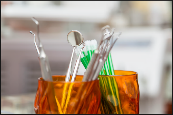 Professional dental hygiene instruments including a mouth mirror, explorer picks, and green toothbrushes.