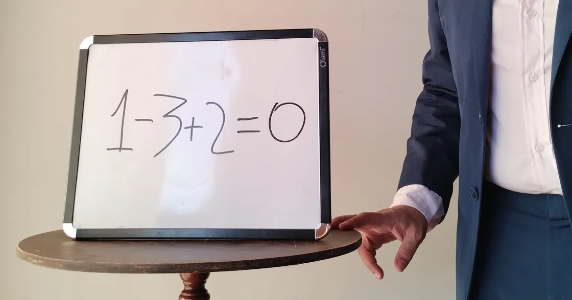 Person standing next to small whiteboard reading "1 - 3 + 2 = 0"