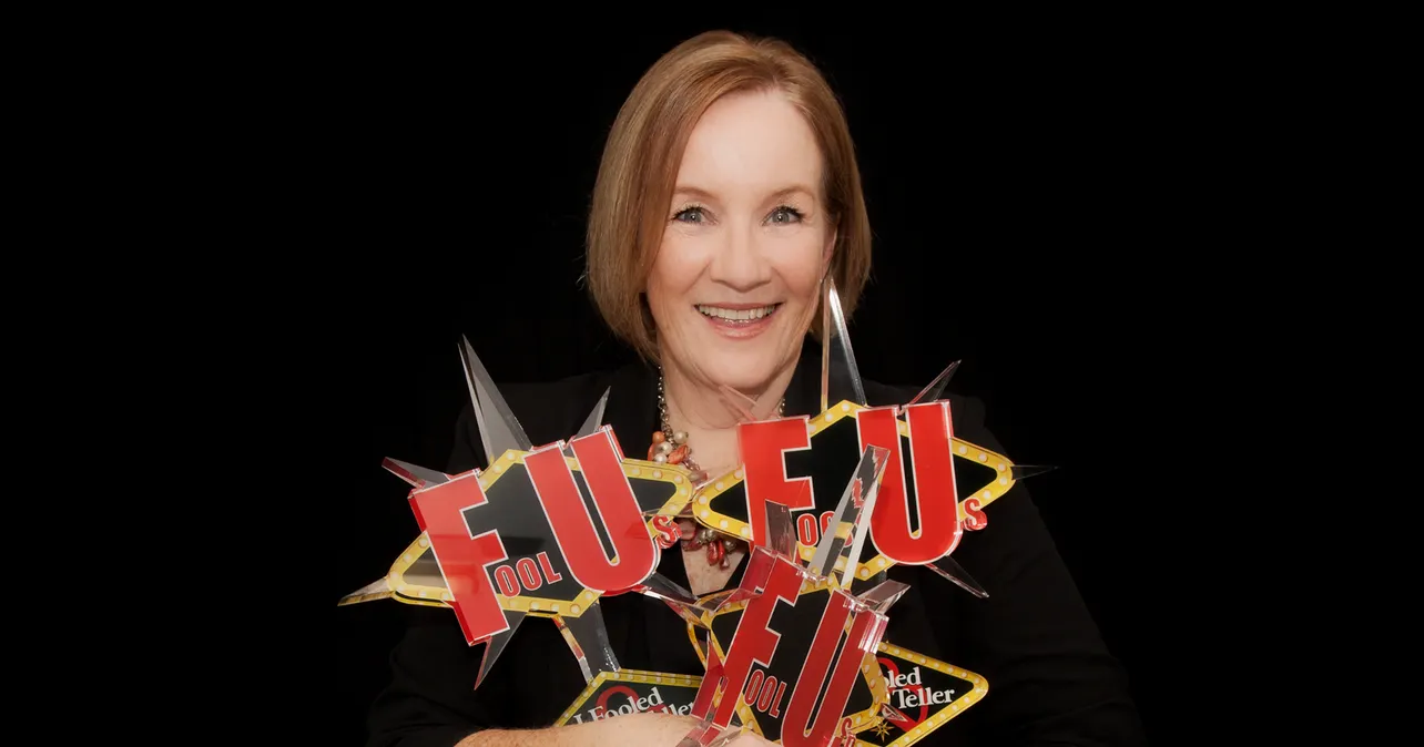 Magician Helen Coghlan smiles while proudly holding multiple Penn & Teller Fool Us trophies against a black background.