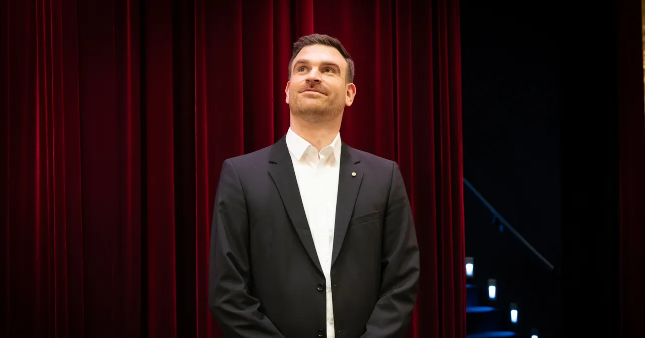 Denis Behr standing in front of a red curtain
