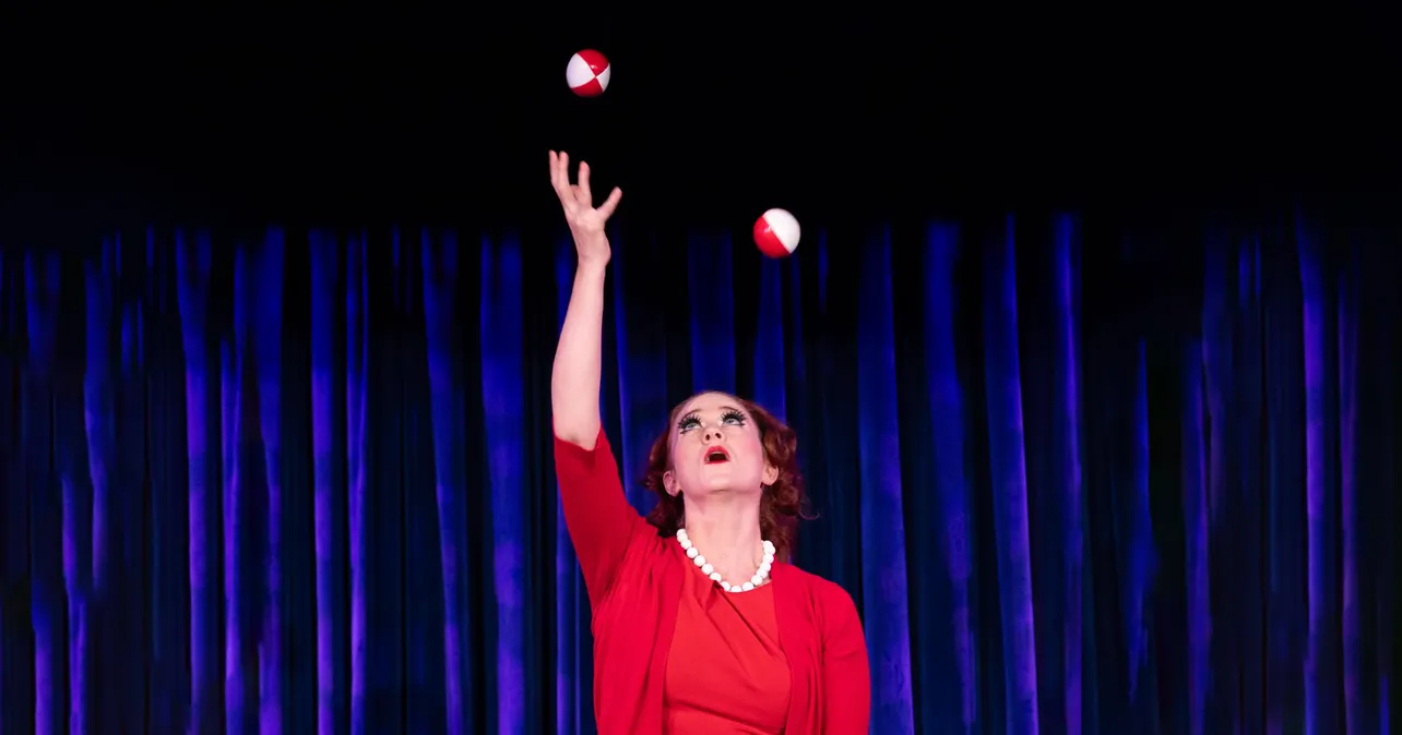 Woman juggling in front of blue curtain