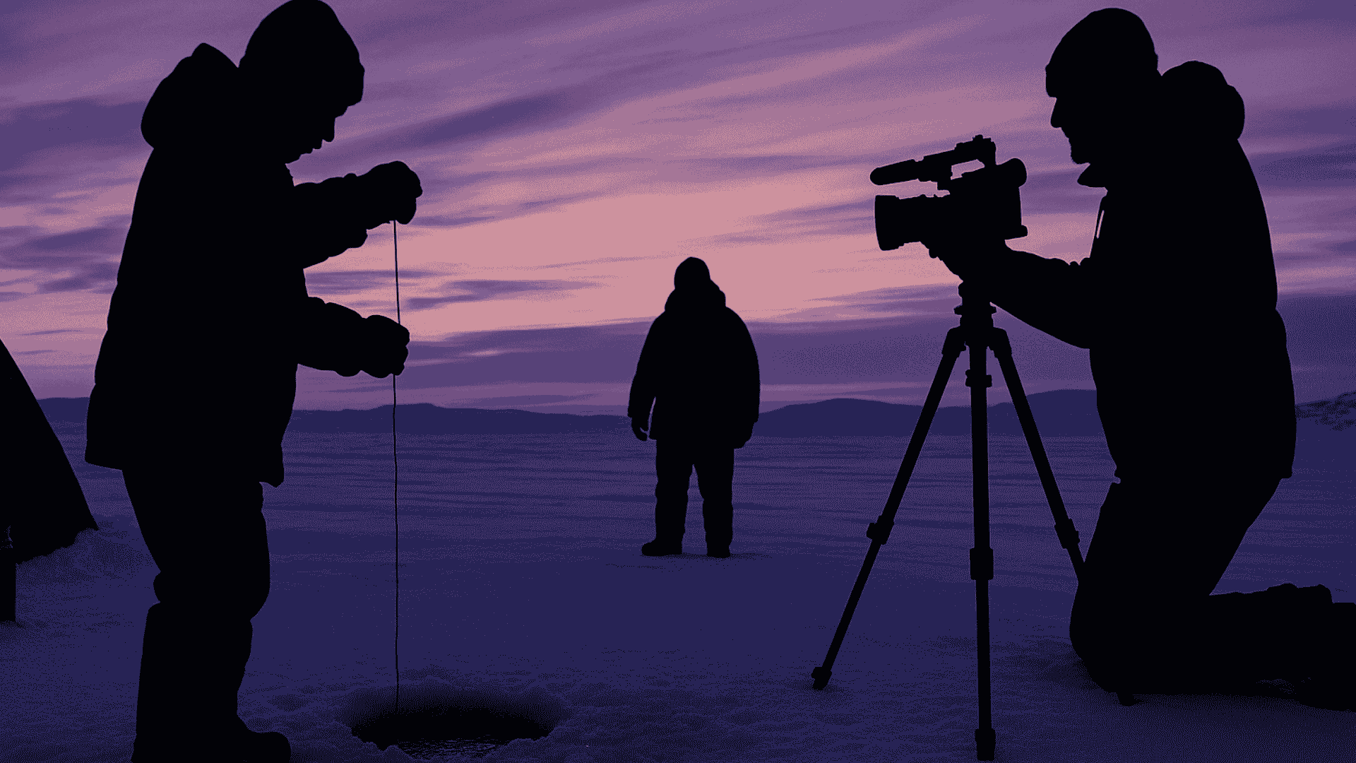 Silhouetted boy ice fishing with camera crew filming nearby at dusk on snowy Arctic tundra.