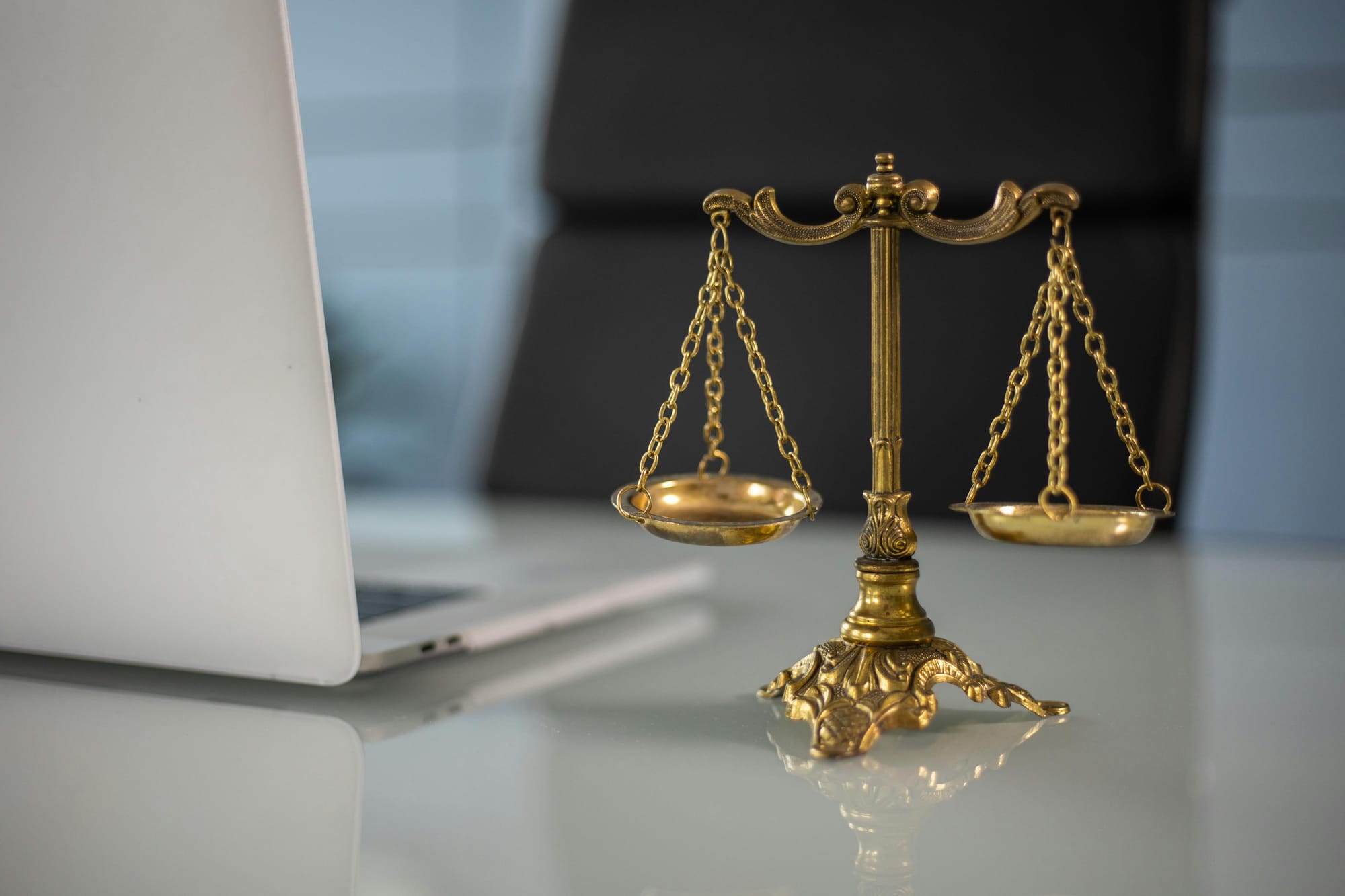 A scales of justice ornament on a desk beside a laptop, symbolising legal and ethical requirements for professionals.