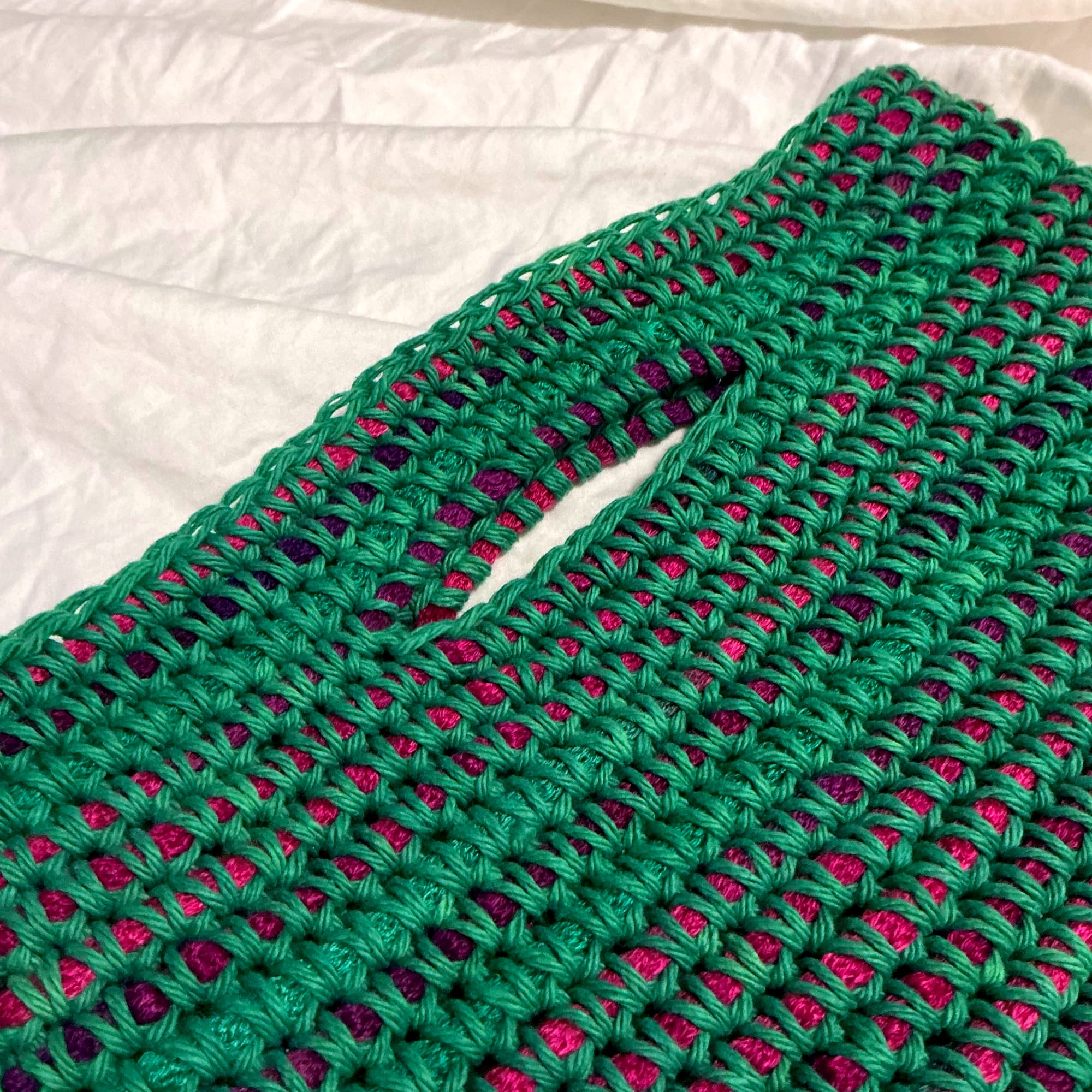 A close up of the handles of the bag. It's a purple and green gradient chunky yarn wrapped with green cotton yarn. 